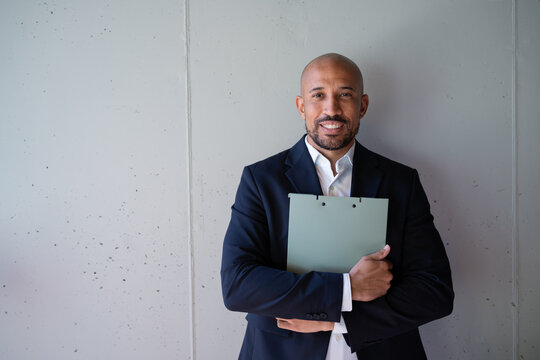 Smiling businessman in suit holding folder against concrete wall