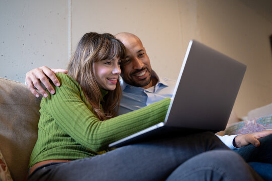 Smiling couple hugging and relaxing with laptop at home