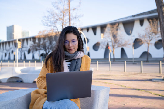 Businesswoman in scarf working remotely on laptop outdoors