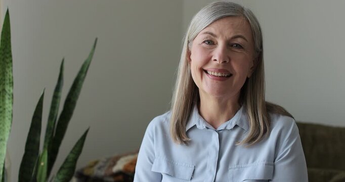 Senior grey-haired woman waving hand talking to webcam video conference calling, online chat meeting at home.