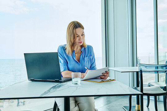 Businesswoman writing on a clipboard by a window with an ocean view