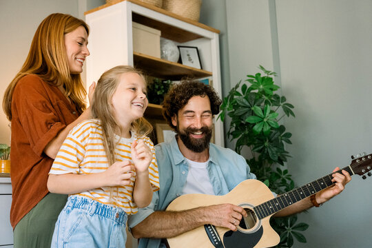 Father playing guitar while family dances and laughs together at home