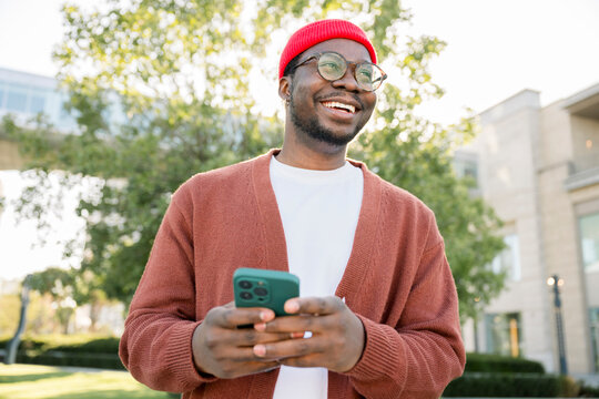 Smiling man outdoors using mobile phone on a sunny urban day