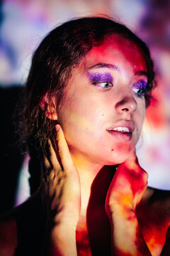 Portrait of teenage girl with glitter makeup in colorful projector light