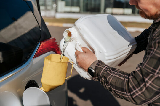 Pouring reserve fuel into car tank with canister and funnel outdoors