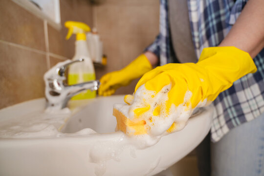 Housekeeper cleaning bathroom sink with rubber glove and sponge