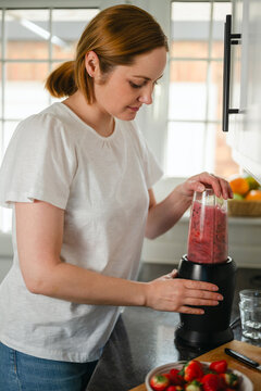 Woman making a fresh berry smoothie in the kitchen for a healthy lifestyle