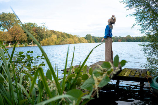 Woman standing on jetty and tossing hair in front of lake