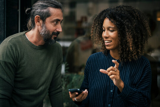 Young businesswoman holding smartphone and suggesting ideas to friend