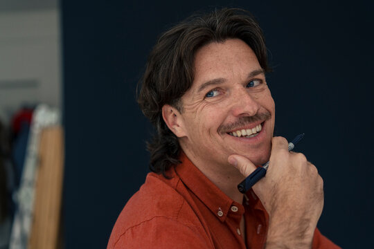 Happy mature man with hand on chin holding pen