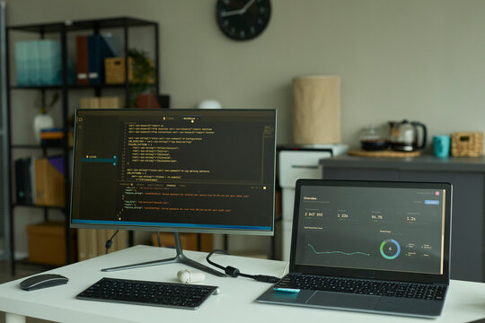 Desk with computer monitor showing code and laptop with chart