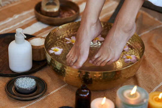 Woman soaking her feet in golden bowl with warm water and flower