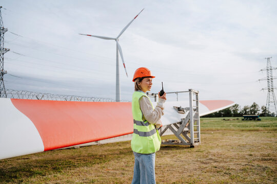 Engineer with reflective jacket and safety helmet standing near wind blade at field
