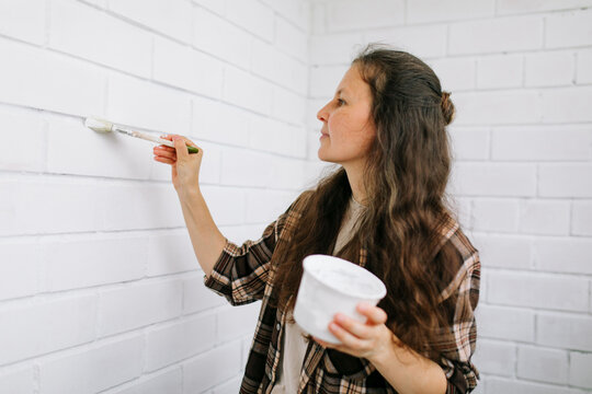Homeowner painting white brick wall indoors for renovation