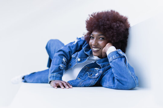 Smiling portrait of woman with afro hairstyle wearing casual denim lying down in studio