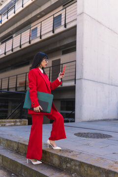Businesswoman in red suit walking on outdoor stairs with smartphone