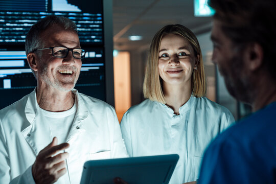 Smiling doctor discussing data analysis on digital tablet at night