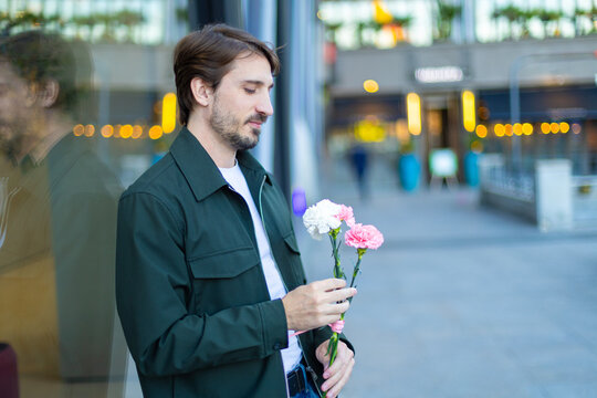 Man holding carnation flowers while waiting thoughtfully in the city