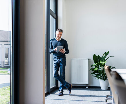 Smiling businessman using tablet standing by office window