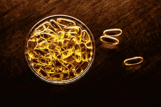 Omega 3 fish oil capsules in a glass bowl on dark wooden table
