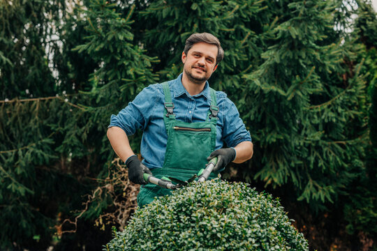 Gardener smiling while trimming a boxwood bush outdoors