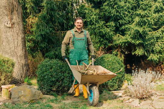 Smiling gardener with wheelbarrow pruning branches in spring