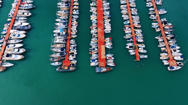 Organized rows of sailboats and motorboats in sea marina. Aerial view of multiple red piers with white boats perfectly aligned in turquoise water.