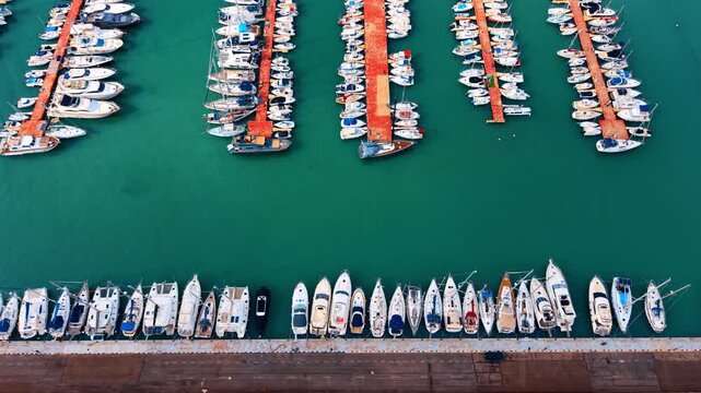 Top down aerial view of boats in marina harbor. White yachts moored at red docks in turquoise sea water.