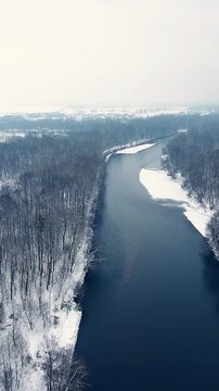 Flying over river surrounded with forest in white winter