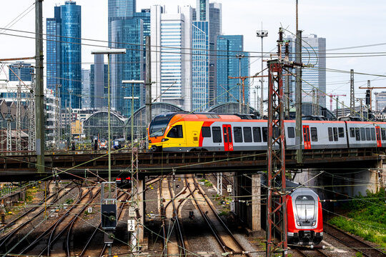 Modern urban transport infrastructure surrounds commuter train on railway tracks by station as frankfurt skyline reflects glass towers