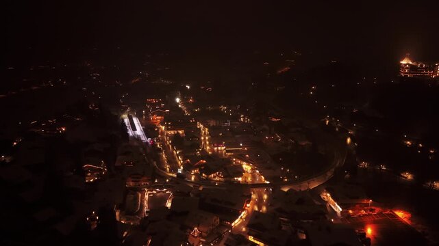 Aerial: downtown Gstaad with snow at night in Canton of Bern, Switzerland, parallax drone shot