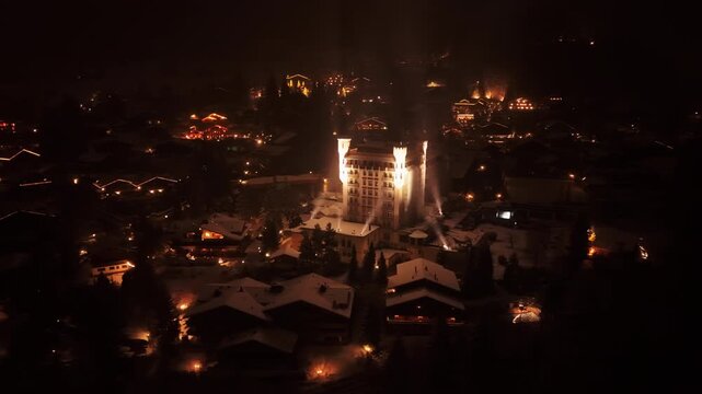 Aerial: close up of Gstaad Palace with light and snow at night in Gstaad, Canton of Bern, Switzerland, orbit drone shot
