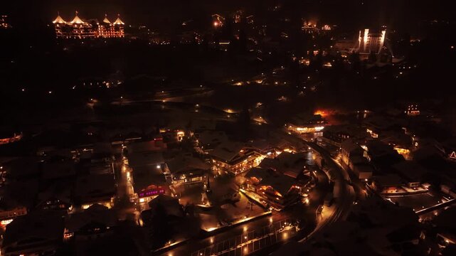 Aerial: townscape and Gstaad Palace with snow at night in Gstaad, Canton of Bern, Switzerland, orbit drone shot