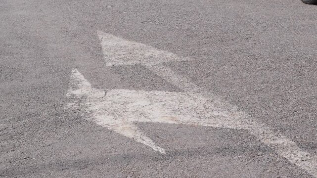 Worn, white double-direction arrows painted on textured asphalt, captured in a close-up shot with natural daylight and no people present.