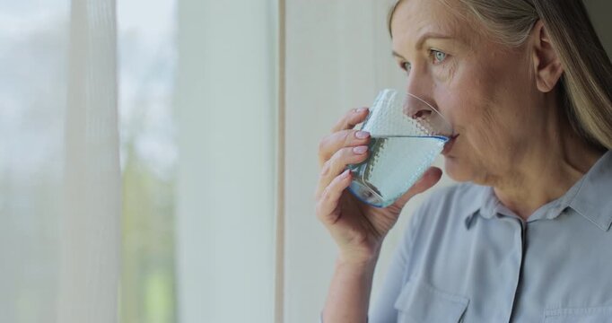 Close up healthy old woman drinking water for healthcare or natural vitamins in a house. Senior person refreshing with liquid for energy or hydration.