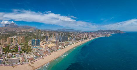 Fototapeta premium Panoramic aerial view of Benidorm, Spain, showcasing the iconic skyline of high-rise buildings along Levante Beach with turquoise Mediterranean waters and mountain backdrop