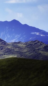 Rolling hills meet towering peaks under a vast blue sky. Sunlight dances on the slopes, creating a peaceful atmosphere in this untouched natural paradise.