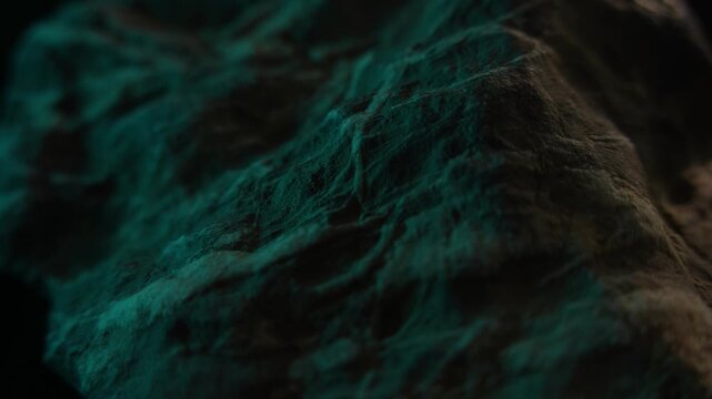 Close-up dark rock surface with green light and rugged texture