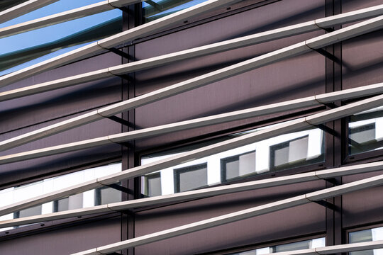 Contemporary architecture facade detail where glass reflection meets slats shadow and modern abstract lines pattern forming a graphic urban surface background