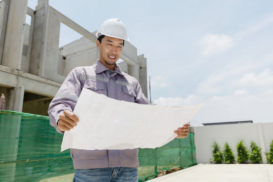 A construction manager inspects a building site, pointing at the structure while holding plans