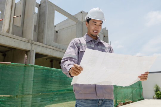 A construction manager inspects a building site, pointing at the structure while holding plans