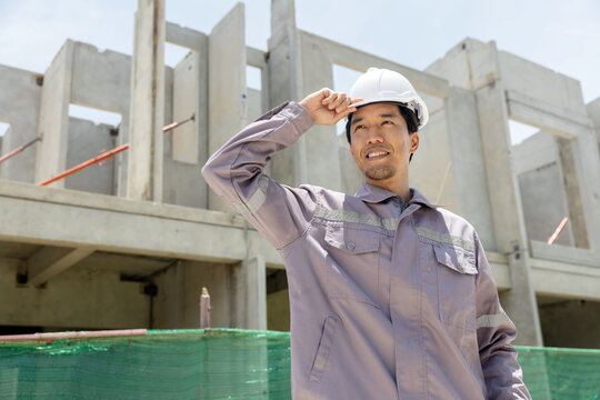A construction manager inspects a building site, pointing at the structure while holding plans