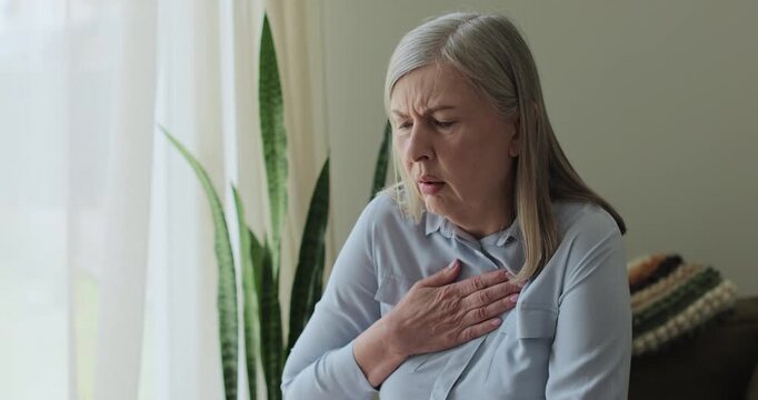 Senior woman, chest inflammation and cardiovascular emergency in lounge, panic attack and physical symptoms.