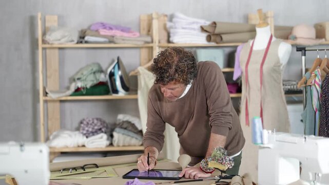 Adult male tailor draws pattern using tablet in sewing workshop
