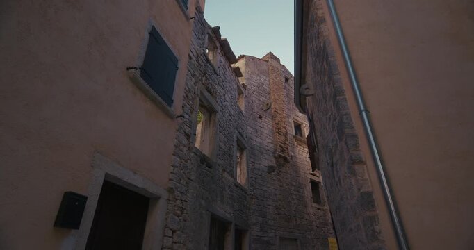 Shot of old stone buildings seen from a narrow passage in Bale, Istria, Croatia. The scene shows stone walls, windows, shutters and a drainpipe between closely spaced buildings.