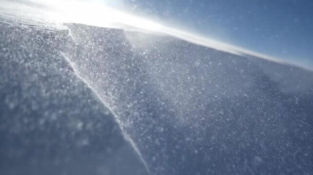 Close-up of snowdrift with blowing snow and sunlight creating backlit particles against a bright blue sky and crisp winter atmosphere