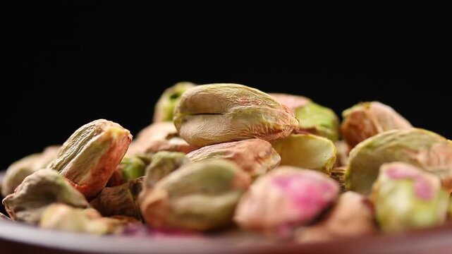 Pile of roasted shelled pistachio kernels rotating slowly on black background. Close-up view