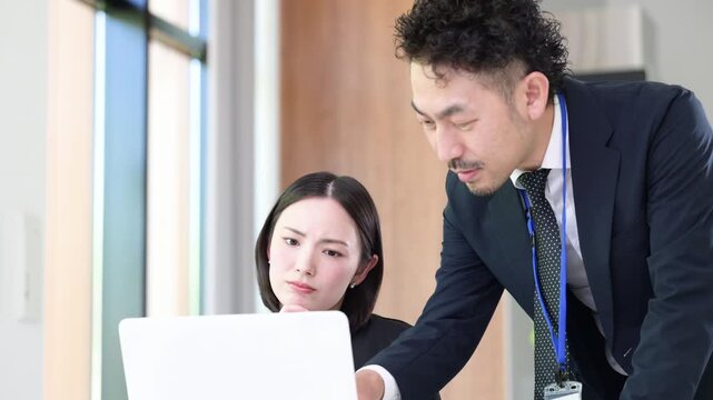 パソコンの前で真剣な表情で考える悩むデスクワーク業務に取り組む上司と部下の男女のビジネスマンチーム　この問題、課題どうしようかな～の動画