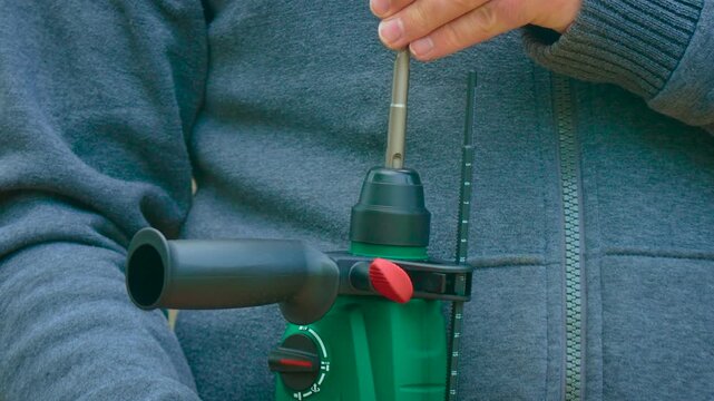 Worker inserting concrete drill bit into hammer drill with SDS chuck close up. Construction tool setup and equipment preparation for drilling masonry surface detail. DIY repair maintenance workshop