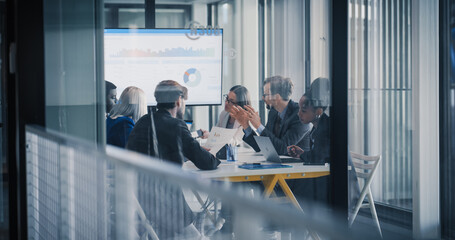 Business Leaders Sit Around a Conference Table Reviewing Charts on a Large Screen, Debating Results, Setting Priorities, and Planning Next Steps While Using Laptops, Printed Reports, and Notes During © Gorodenkoff